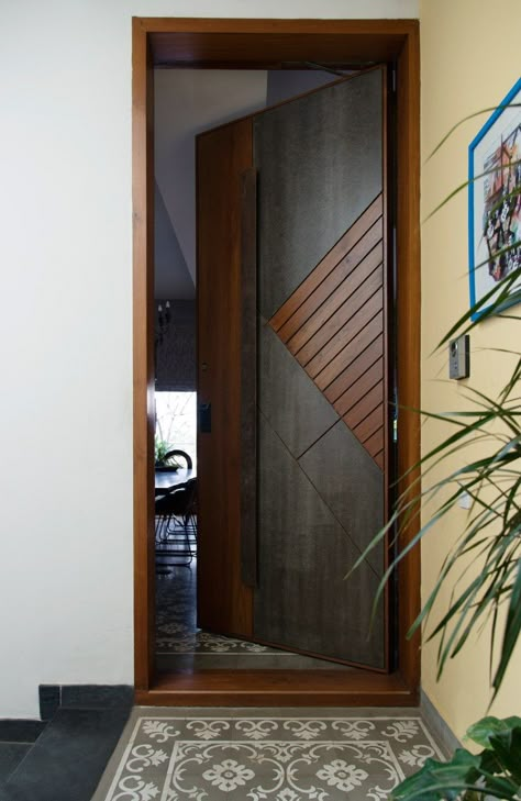 A subtle yellow wall leads to the main door of the house finished in stone and wood while the patterned tiles act as a faux rug. Photography by Prachi Damle Tor Design, Pintu Interior, Wooden Door Entrance, Flush Door Design, Modern Entrance Door, Modern Wooden Doors, House Main Door Design, Main Entrance Door Design, Front Door Design Wood