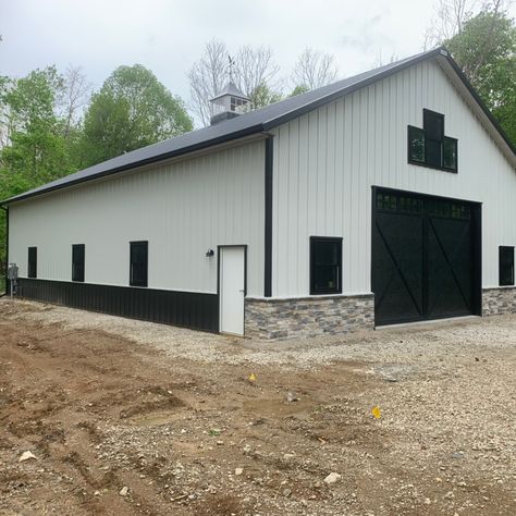 This beautiful pole barn storage building is set back on top of a hill in a secluded wooded area in Central Ohio. The white sidewalls with black trim and stone wainscot on the front of the building really make the building shine. The custom 4-sided cupola on top of the building provides for a source of natural lighting inside the building.   The building is 42' x 64' with over 14' in height for storage of an RV, boat, trailers and other toys. Pole Barn For Boat Storage, White And Black Metal Building, White Metal Shop With Black Trim, White Metal Shop Building, White And Black Metal Shop, White Shop With Black Trim, White Metal Building With Black Trim, Black And White Shop House, White And Black Shop House