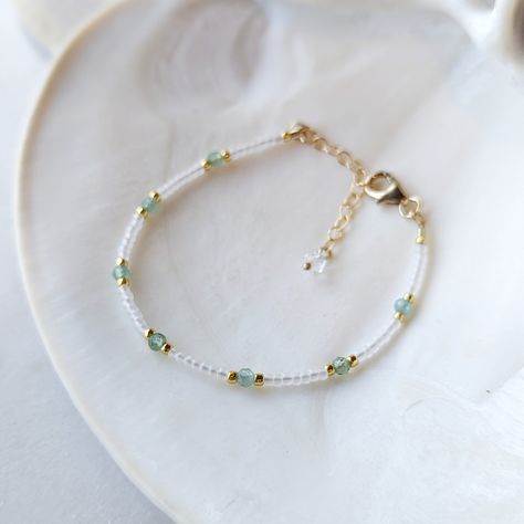 Like the clear teal waters of a tropical destination - this *rare* Aqua Teal Green Apatite bracelet is absolutely dreamy! The Aqua Teal Green Apatite gemstones have the most captivating transparent teal color to them. And they are not something you can find very often. They are paired with semi-transparent pearlescent glass beads for the ultimate beachy look! SHOP THE MATCHING NECKLACE! Just like water, Green Apatite has the power to purify, cleanse and calm. It is also an empowering stone of manifestation. It can give you greater inner strength, inspiration and clarity. It can help you tune in to your intuition, so that you can begin making decisions with confidence. Colors: This beaded bracelet features semi-transparent matte glass beads in the most alluring pearlescent white color Gemst Teal Bracelet Ideas, Tropical Beaded Bracelets, Clear Bracelet Ideas, Small Bead Designs, Teal And Gold Jewelry, Transparent Beads Necklace, Bracelet Ideas Beaded Inspiration, Clear Bead Bracelet, Double Beaded Bracelets