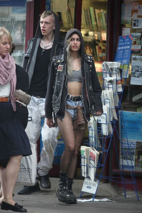 Super edgy sleaze punk fashion from Alice Dellal, wearing a cutoff leather jacket, denim shorts, ripped fishnets and grungy combat boots