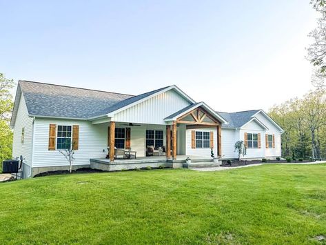 A home that embodies farmhouse decor can come in many styles, but wood accents on the exterior create an unbeatable look. White siding covers this home and welcomes wooden shutters and pillars. A wooden truss and matching beams are showcased at the entrance of this home, supporting a gable roof...   Image: hickoryridgecharm Wooden Shutters On White House, Vinyl Siding Wood Accents, White Siding Wood Accents, White Siding Exterior With Wood Accents, Wood Gable Accents, White Houses With Wood Accents, All White House Exteriors Farmhouse, Exterior Paint Colors For Concrete House, White House With Wooden Shutters