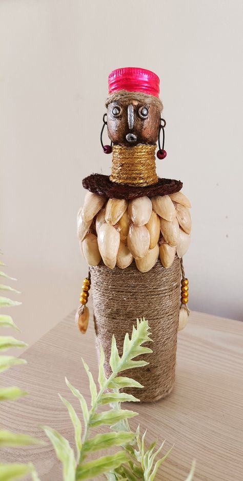 African Doll using a waste plastic bottle, jute rope and pistachios shells Pista Shell Bottle Art, Hajmola Bottle Diy, Theyyam Bottle Art, Mouldit Clay Art On Bottle, Easy Bottle Art With Clay, Diy African Dolls, Pista Shell Crafts, African Doll, Pistachio Shells