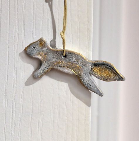 "A cute little grey squirrel hanging ornament. The cute critter I hand sculpted and textured in a primitive style, from artist grade polymer clay, and finished off with brushed on gold, black and white metallic mica powders, a pewter coloured crimp bead for his eye, and a clear coat satin sealer to enhance and protect his surface. Finally, he is strung on knotted gold or beige coloured cotton cord and topped off with a grey organza ribbon bow. Makes a perfect add on gift adornment or as a small Fimo, Christmas Ornaments Pottery, Ceramic Squirrel, Pink Doors, Bells Ornaments, Squirrel Ornament, Hygge Design, Christmas Ceramics, Grey Squirrel