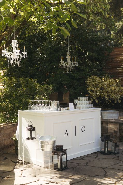 Old Hollywood Glamour Small Backyard Wedding. Self serve bar. DIY wedding bar. White bar with black monogram initials and chandeliers hanging from trees. Backyward wedding bar Elegant Wedding Bar Set Up, Custom Bar For Wedding, Old Hollywood Outdoor Wedding, Engagement Party Location Ideas, Wedding Cocktail Bar Ideas, Wedding Bar Details, Simple Elegant Backyard Wedding, Wedding White Party, Classic Old Hollywood Wedding