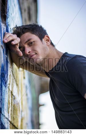 Attractive young man standing leaning against colorful graffiti wall, looking at camera Leaning Down Pose, Leaning Against Wall Pose Reference, Against Wall Pose, Leaning Against Wall, Colorful Graffiti, Billionaire Romance, Romance Series, Just Pretend, Man Standing