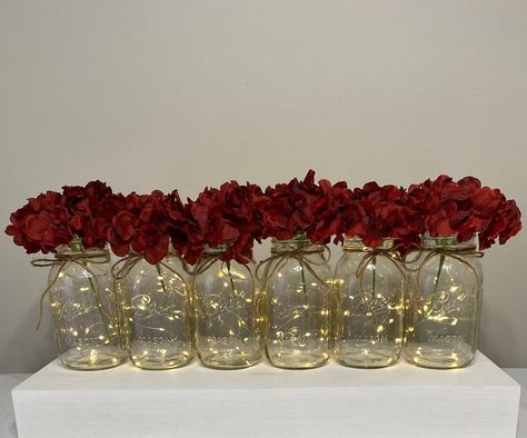 This listing includes 6 beautiful quart mason jars with fairy lights, twine bows and artificial flowers. We have many flower options to choose from. Wine red  Hydrangeas shown in first photo. You can get color ribbon instead of twine, just message us. These lighted mason jars are the perfect wedding table centerpieces and can be used for bridal showers, baby showers or home decor! Quart mason jars are 6.9 inches tall by 3.5 inches wide. The lights have a on/off switch and have replaceable cr2032 Fairy Light Mason Jars, Centerpieces Burgundy, Mason Jars Wedding, Xv Ideas, Red Centerpieces, Red Wedding Decorations, Red Wedding Theme, Party Table Centerpieces, Red Rose Wedding