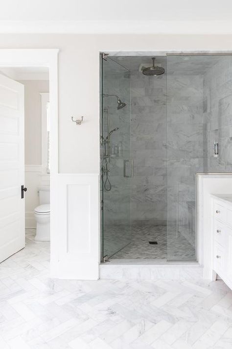 Gray marble herringbone floor tiles lead to a seamless glass shower boasting a rain shower head mounted to a gray marble tiled ceiling framed by gray marble surround tiles. Herringbone Floor Bathroom, Grey Marble Bathroom Tiles, Herringbone Shower Floor, Herringbone Floor Tiles, Bathroom With White Cabinets, White Tile Flooring, Herringbone Bathroom Floor, Tiled Ceiling, Marble Herringbone Floor