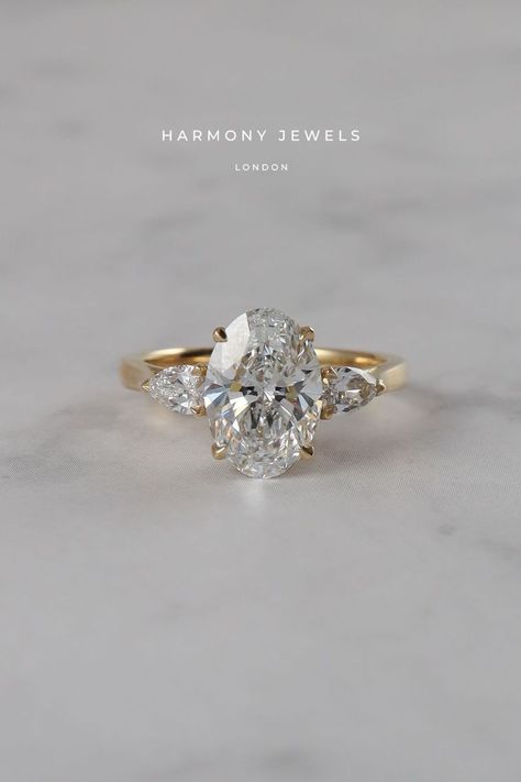 Side Stone Wedding Rings, Harmony Jewels London, 3 Stone Oval Engagement Ring Yellow Gold, Gold Oval Engagement Ring Side Stones, Oval Ring With Accent Stones, Oval Diamond Side Stones, 3 Stone Setting Engagement Ring, Soft Gold Engagement Ring, Oval Ring Pear Side Stones