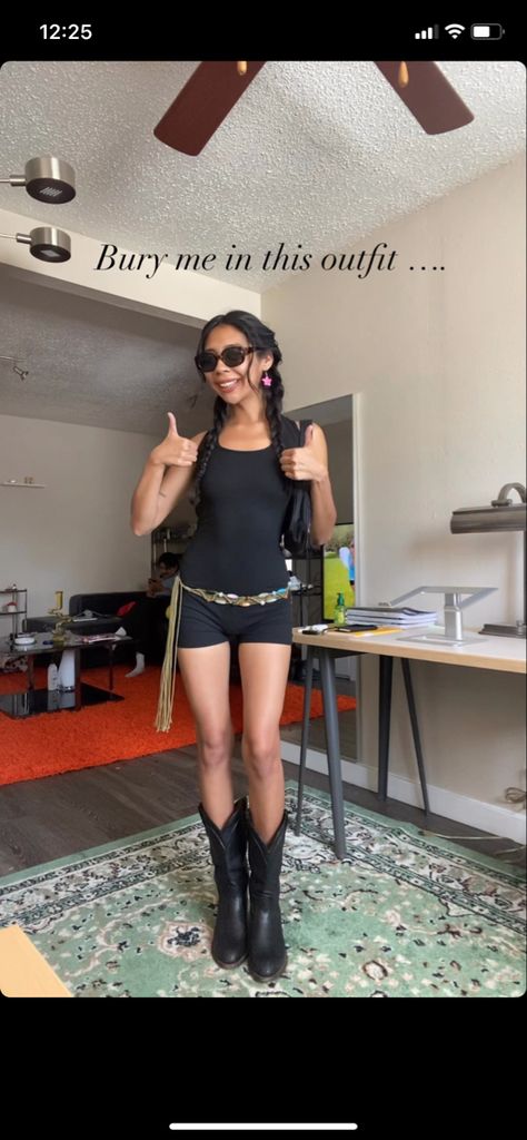 Girl is wearing a black romper with black cowboy boots. She has a western style belt adorned with different colored crystals tied at her waist with a  tassels/fringe. She has a  “God’s Favorite” purse from Praying. She also had pink star dangly earrings. She is posing with her thumbs up. The caption reads “Bury me in this outfit..” Romper Outfit Festival, Romper Festival Outfit, Romper And Cowboy Boots, Romper With Cowboy Boots, Cowboy Boots Outfit Y2k, Long Shorts Cowboy Boots, Y2k Cowboy Boots, Cowboy Boot Outfits Grunge, Romper With Boots