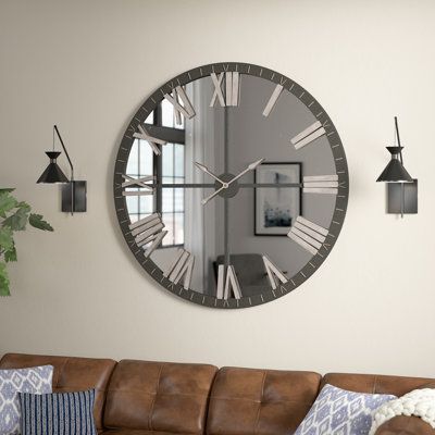 When decorating your home, it’s always considered a win-win when something is both fashionable and functional. Take this wall clock for example: Made in the USA from metal, the frame showcases a round silhouette with a mirrored face, offering some subtle shine to your space. Powered by one AA battery (not included), two spaded hands point to Roman numeral hours, lending some understated appeal to your arrangement. Plus, this piece is sure to make a statement on any bare wall in your abode. | Tre Living Room Wall Decor With Clock, Clock Decor Living Room, Large Round Wall Clock, Large Wall Clock Decor, Unique Living Room Furniture, Living Room Wall Clock, Metal Living Room, Large Wall Clock Modern, Wall Clocks Living Room