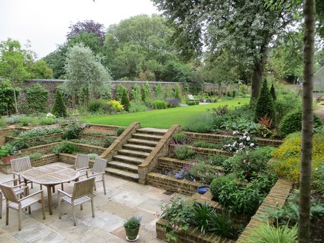 This gorgeous sunken patio is remniscent of victorian times. I love the terraced beds and stairs leading to a lush lawn. #sunkenpatio #patiodesignideas #stonepatio Tiered Landscape, Sunken Patio, Terraced Landscaping, Terraced Backyard, Sloped Backyard, Backyard Garden Landscape, Tiered Garden, Sloped Garden, Garden Steps