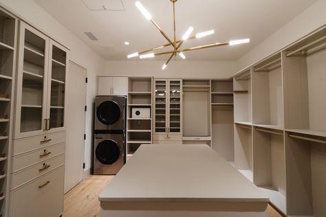 Antique burnished brass chandelier in Master custom closet in Los Altos Hills Home with island storage and washer and dryer. Custom closets by California Closets. #thedendesigngroup #mastercloset #customcloset #bayareainteriordesign #closetlighting #chandeleir #brasslighting #brasschandelier Walk In Closet Ideas With Laundry, Walkin Closet With Washer And Dryer, Master Closet Design With Laundry, Walk Through Closet To Bedroom Master Suite Layout, Washer And Dryer In Master Closet, Walk In Closet With Washer And Dryer, Master Closet With Washer And Dryer, Laundry In Master Closet, Closet With Washer And Dryer