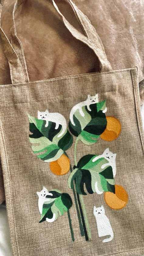 A beige tote bag has white cats hanging on leaves painted on it. Paint Your Own Tote Bag, Canvas Tote Bag Painting Ideas, Toat Bag Painting Ideas, Painted Canvas Tote Bags, Painting A Tote Bag, Hand Painted Canvas Bags, Canvas Bag Design Art, Drawing On Bags Ideas, Painting On Bags Ideas