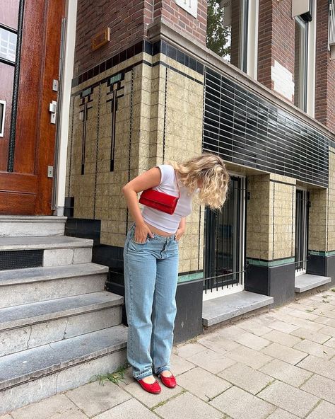 Girl in Amsterdam wearing a white baby tee, low waist straight blue jeans, bright red ballerinas, and a bright red bag, exploring the city streets. White And Red Shoes Outfit, Outfit Ideas Red Shoes, Outfits With Pops Of Red, Jeans And Red Flats Outfit, Red Flat Outfits, Red Bags Outfit, Red Flats Outfit Ideas, Red Bag Outfit Summer, Red Ballerina Flats Outfit