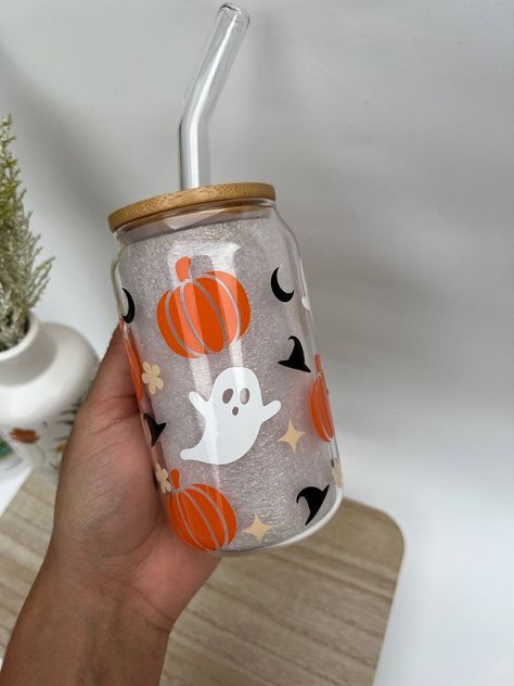 Enjoy your favorite Halloween drinks in style with our custom Halloween glass cup with bamboo lid and straw. This cup is perfect for iced coffee, bobba tea, and other cold beverages. It is also great for everyday use or as a gift for friends and family. Our Halloween glass cup is made of high-quality glass, which is durable and dishwasher safe. The cup features a variety of Halloween-themed designs, such as ghosts and pumpkins. The cup also comes with a bamboo lid and glass straw, making it perfect for on-the-go use. Each order is handmade to order, actual product may differ slightly from picture. Colors may vary slightly due to computer monitor settings. - BPA Free - Durable and dishwasher safe -Comes with a bamboo lid and glass straw HOW TO TAKE CARE OF IT:  To ensure that your glass can Halloween Iced Coffee Cup, Halloween Glass Tumblers, Coffee Glass Cup Design, Halloween Glass Cups, Halloween Cup Ideas, Halloween Party Cups, Ghost Cup, Pumpkin Cups, Christmas Cups