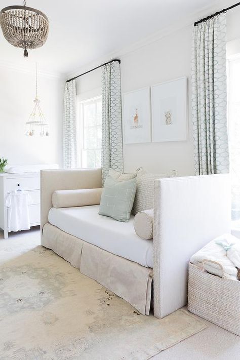 A taupe beaded chandelier lights a beautifully designed gender-neutral nursery featuring a beige striped skirted daybed accented with gray and beige pillows and placed on a gray faded vintage rug beneath framed animal photographs. Nursery Room With Daybed, Nursery Daybed, Baby Blue Curtains, Transitional Nursery, White Faux Fur Rug, Costal Bedroom, White Daybed, Grey And White Bedding, Vintage Crib