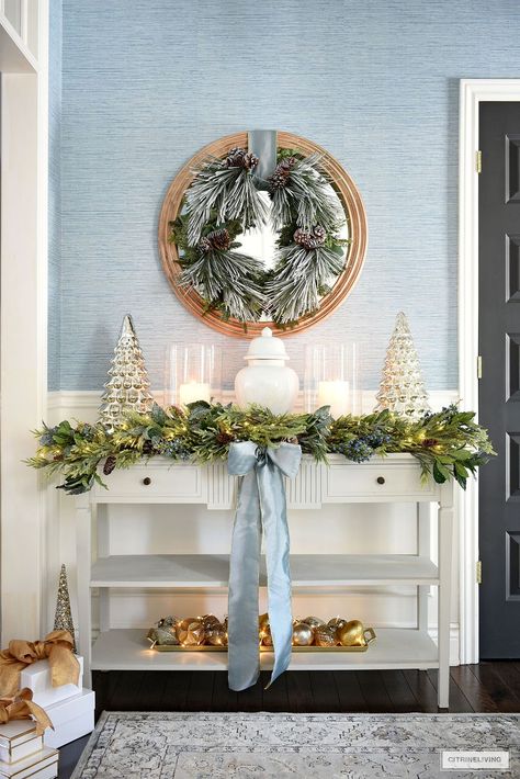 Console table styled for Christmas with a white ginger jar, glass hurricanes and mercury glass trees on either side. Lush greenery garland and frosted wreath. A classic grandmillenial home. Mercury Glass Trees, Christmas Entryway Decor, Glass Trees, Christmas Entryway, Blue Christmas Decor, Christmas Decor Inspiration, Christmas Tablescape, Christmas Time Is Here, Aesthetic Christmas