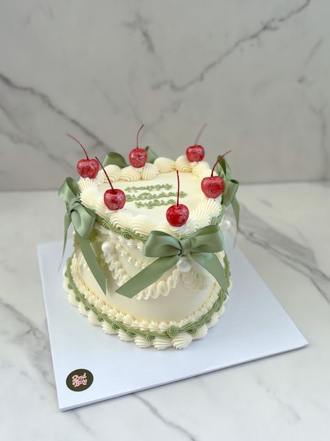 White vintage heart cake with sage green bows and cherries Vintage Heart Cake With Cherries, Summer Bday Cakes, Vintage Cake Decor, Cherry Vintage Cake, Pastel Vintage Cake, Sage Green Heart Cake, Birthday Cake With Bows, Sage Green Cake Ideas, Vintage Bento Cake