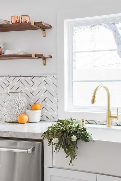 A farmhouse sink with a brushed gold gooseneck faucet is positioned beneath a window partially framed by white herringbone tiles. Chevron Backsplash, White Herringbone Tile, White Kitchen Backsplash, Tile Design Pattern, Kitchen Tiles Design, Glass Tile Backsplash, White Backsplash, Glass Backsplash, Herringbone Tile