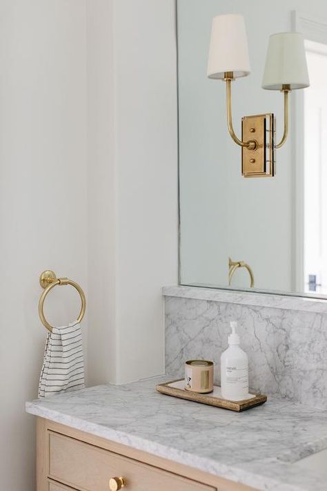 Bathroom features brass Hulton sconces on an arched vanity mirror over a tan French washstand with a gray marble countertop and backsplash and brass towel ring. Marble Countertop And Backsplash, Marble Backsplash Bathroom, Vanity Backsplash, Block Print Wallpaper, Kate Marker Interiors, Grey Floor Tiles, White Shiplap Wall, Grey Headboard, Arched Mirror