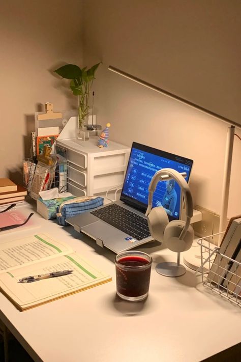 A minimalist study desk setup with a laptop, open notebook, reading lamp, headphones, and a calming candle. The desk also includes books, a plant, and organizational drawers, creating a warm and inviting space perfect for studying or working Simple Study Table Ideas Student, Simple Office Setup, Simple Desk Organization, Student Desk Setup, Minimalist Study Table, Setup Notebook, Simple Desk Setup, Simple Desk Organizer, Study Desk Setup