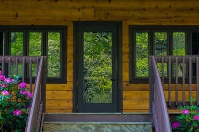 Log home with black trim front door Log Cabin Entry Doors, Log Cabin Black Roof, Log Cabin Trim Colors, Log Home Exterior Colors, Rustic Bathtubs, Log Homes Exterior, Black Window Trims, Log Cabin Exterior, Black Exterior Doors