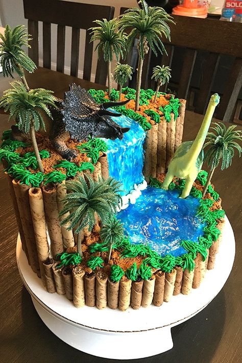 Throwing a dinosaur themed birthday party for your boy - or girl? This easy dinosaur birthday cake will blow the pants off everyone. From a 3rd birthday to a 20th, this awesome-looking cake can be appreciated by any dino fan. A homemade dinosaur cake has never been easier, even with the DIY waterfall! This dinosaur cake uses NO fondant, it's strictly buttercream, sparkle gel, and a couple of cookies. (No one will even mind that the dinosaurs and trees are plastic, because it looks cool anyway.) Dinosaur Cakes For Boys, Birthday Cake Diy, Dino Birthday Cake, Dinosaur Birthday Cake, Dinosaur Birthday Theme, Jurassic Park Birthday, Dino Cake, Dinosaur Birthday Cakes, Cake Diy