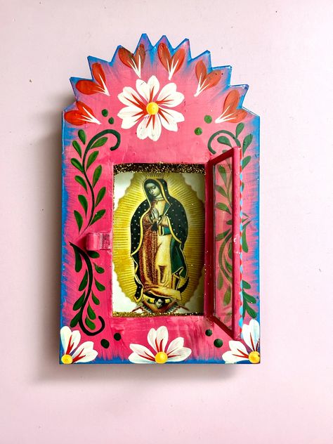 Dimensions: 6"x4"x1" This authentic Mexican Tin Nicho with a hinged glass door is beautifully hand crafted and hand painted  by a high skilled Mexican Artisan.  It  comes with a image of Virgen de Guadalupe in the inside, which you can change for a photo of a deceased loved one as a tribute.  Our Lady of Guadalupe, commonly known as the Virgin of Guadalupe, (Spanish: Virgen de Guadalupe) is a catholic title of Mary , mother of Jesus, associated with a series of 5 apparitions to a Mexican peasant named Juan Diego, which are believed to have occurred in December 1531. This special and outstanding item will make a splendid addition to your Altar or anytime gift for your loved ones.    Uses for this beautiful and unique piece of Mexican folk art include : Wall hanging decor, gifts to family an Mexican Shadow Boxes, Mexican Folk Art Decor Diy, Mexican Nichos, Mexican Catholic Art, Latin American Folk Art, Mexican Folk Art Decor, Mexican Folk Art Painting, Mexican Wall Decor, Mexican Paintings