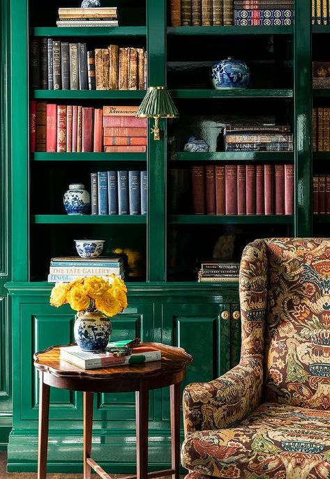 Living room features a glossy emerald green built-in bookcase with cabinets that boast brass knobs, a brown flocked wingback chair and a round wooden accent table. Green Built In Bookcase, Bookshelf Color Ideas Paint, Timeless Homes, Calke Green, Apartment Refresh, Green Bookshelves, Academia Library, Library At Home, Green Library