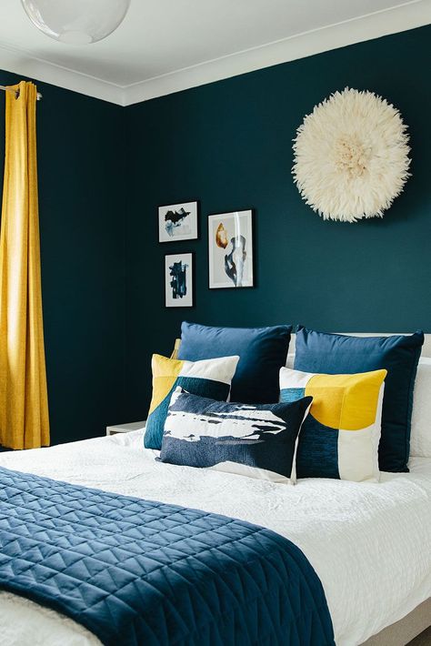 We love using dark blues to warm up a space. The pops of sunshine yellow in this bedroom scheme also add a welcome contrast and bring some energy back to the space - perfect for those mornings in the Autumn and Winter time where you might need a bit of encouragement out of bed! This room is so beautifully decorated that it could be a 5-star hotel room! Click the link to see how you can make your master bedroom so beautiful that you'll never want to leave! 🛏️ Guest Bedroom Ideas Black, Bedroom Blue And Gold, Bedroom Ideas Black And White, Dark Blue Bedroom Walls, Blue Yellow Bedrooms, Dark Blue Rooms, Bedroom Ideas Black, Teal Rooms, Guest Bedroom Ideas