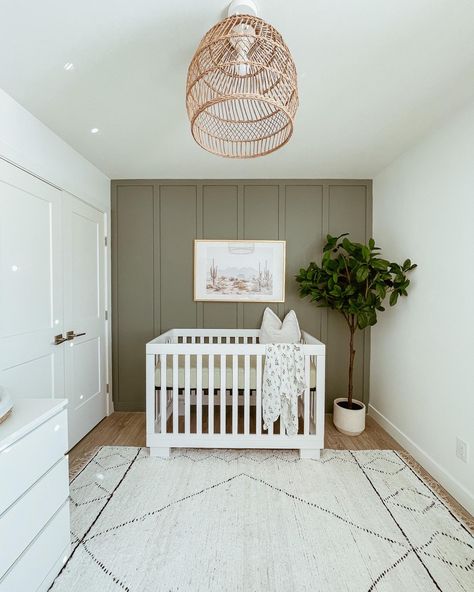 Green feature wall with wicker light fixture and textured rug; plant, white crib, boho art Olive Green And Grey Nursery, Sage Green Nursery With White Crib, White Wicker Nursery, Green Feature Wall Nursery, Sage Green And White Nursery, Green White Nursery, Nursery Ideas White Crib, Plants For Nursery, Nursery With White Crib