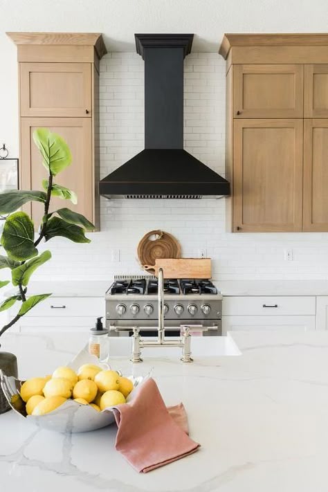 Stacked brown kitchen cabinets flank a black range hood mounted to white subway backsplash tiles over a stainless steel oven range placed between white shaker cabinets topped with a white quartz countertop. Black Range Hood, Kitchen Vent Hood, Oven Hood, Hood Ideas, Brown Kitchen Cabinets, Kitchen Vent, Stainless Steel Stove, Black Range, Kitchen Hood