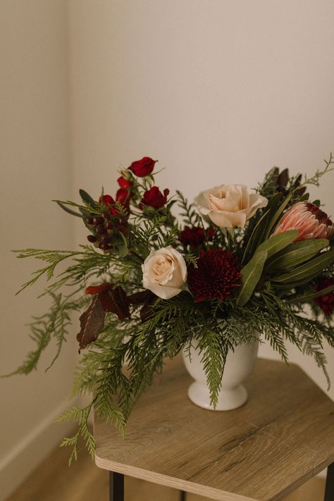 This beautiful “Gather" arrangement features a stunning protea mixed with gorgeous burgundy florals and mixed winter greens. The perfect floral addition for your holiday décor. Variations may occur according to availability. Order at least one week in advance for best match. Christmas Party Floral Centerpieces, Holiday Party Floral Centerpieces, Christmas Dried Floral Arrangements, Floral Arrangements Winter, Holiday Flowers Arrangements, Simple Christmas Floral Arrangements, Holiday Floral Centerpieces, Bowl Floral Arrangements, Holiday Flowers