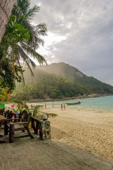 A moody view of the changing weather on one of the best beaches in Koh Phangan. This tropical island view showcases a waterfront restaurant that sits on a white sandy beach with the crystal clear turquoise water of the Gulf of Thailand. Long tail boats, the typical Thailand boat, sit in the water with palm trees and the lush jungle in the background. Travel Aesthetics, Thailand Vacation, Thailand Adventure, Full Moon Party, Thailand Trip, Thailand Backpacking, Thailand Travel Tips, Thailand Travel Guide, Thailand Holiday