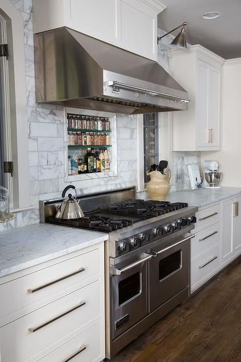 Lovely kitchen features a stainless steel kitchen hood fitted with a pot rack stands over a carrera marble subway tiled backsplash fitted with a tiled spice niche and a stainless steel stove flanked by arched windows illuminated by Boston Functional Library Wall Lights. Spice Niche, Stainless Steel Kitchen Hood, White Kitchen Set, White Kitchen Furniture, Viking Kitchen, Beautiful White Kitchens, White Kitchen Appliances, White Marble Kitchen, Hood Ideas