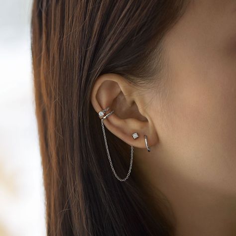 A unique conch ear cuff that features a chain and connected stud earring. Bendable for a snug fit. Sold as a single earring. Sterling Silver Cubic Zirconia, prong setting Hypoallergenic, lead and nickel free Inner diameter 9mm x Band Thickness 1.5mm Crystal 3mm Chain Length 2.75in Bendable for a snug fit #E515-Sx1 Unique Ear Cuffs, Minimalist Ear Piercings, Different Ear Piercings, Unique Ear Piercings, Ear Peircings, Earring Cuff Chain, Ear Cuff Chain, Types Of Ear Piercings, Cool Ear Piercings