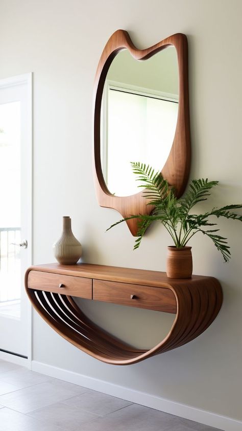 A wall-mounted console table and mirror set. The console table has an organic, curved design resembling a wave or a ribbon, with a flat surface on top for placing objects and an open shelf area underneath. It is made of wood with a rich, warm tone that complements the similarly styled wooden frame of the mirror above it. The mirror has an asymmetrical shape, wider at the top and tapering towards the bottom. By freepik Tiny Front Entry, Small Apartment Entrance, Small Entryway Decor Ideas, Apartment Entryway Decor, Small Open Concept, Mid Century Modern Entryway, Entryway Inspo, Wilfred Owen, Boho Mirrors