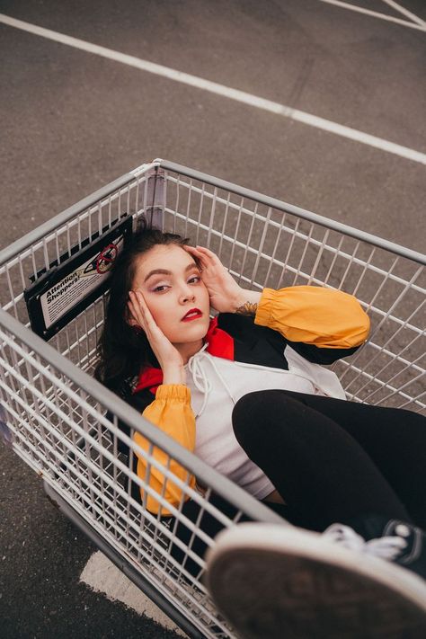 Model is laying in a shopping cart with one leg up, shoe slightly in frame and out of focus. Photographer is shooting from above. Shopping Cart Portrait, Perspective Poses Photography, Street Photoshoot Poses Women, Mood Board Photoshoot, Public Photoshoot, Shopping Cart Photoshoot, Photoshoot Ideas Female, Carpark Photoshoot, Mall Photoshoot