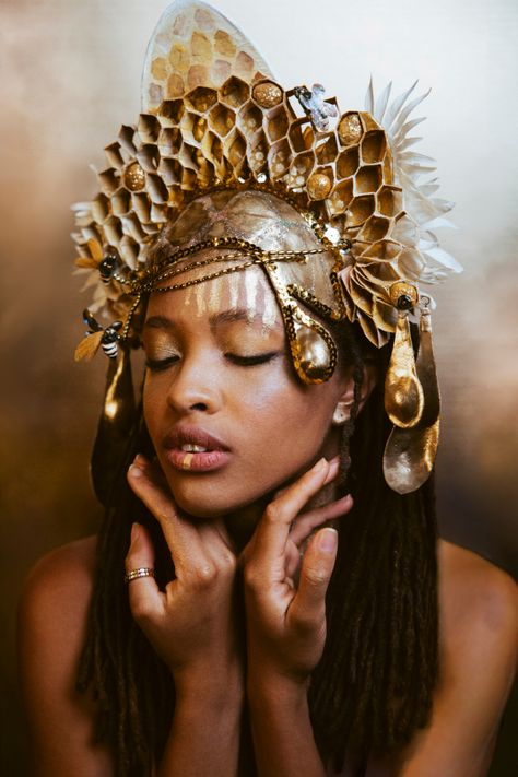 Beautiful woman with caramel skin and dreads wears a feminine, gold honey comb structured crown with gold drips of honey and fluffy white flowers.  She is looking down softly with hands gracefully resting under her chin on a mottled gold backdrop, from the shoulders up. Honey Costume, Gold Headdress, Queen Bee Costume, Theme Carnaval, Crown Headpiece, African Theme, Bee Costume, Bee Dress, Gold Headpiece