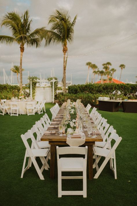 Outdoor Garden Waterfront Wedding Reception with Tropical Wedding Decor, Long Feasting Wooden Tables with Burlap Runners, White Folding Chairs, Against Palm Tree Background | Sarasota Beachfront Wedding Venue Longboat Key Club Backyard Beach Wedding Reception, Garden Chairs Wedding, Wooden Table With White Chairs, White Chair Wedding, Palm Tree Wedding, Tropical Chair Decor Wedding, White Garden Chairs Wedding Reception, White Wooden Chairs Wedding, White Folding Chairs Wedding Reception