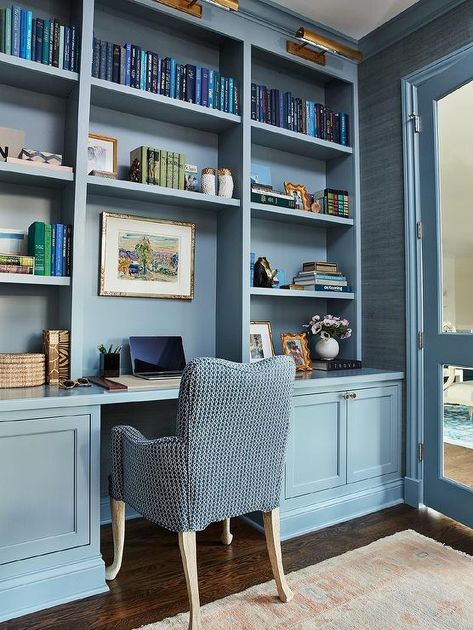 A blue desk chair sits at a blue built-in desk fixed beneath blue built-in bookshelves lit by antique brass picture lights. Blue Built Ins, Garage Remodel Ideas, Remodel Garage, Built In Desk And Shelves, Blue Bookshelves, Den Library, Built In Bookshelves, Bookshelf Lighting, Library Office