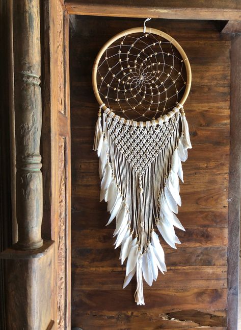 This beautiful large handmade white crochet and macrame dream catcher is a perfect boho wall hanging for home decor. Made with love and good vibes it's perfect for a bohemian bedroom, nursery room, kids bedroom, or living room. Dream catchers originate from Native American cultures. The dream catcher is believed to protect a person from bad dreams.  The good dreams filter down through the feathers and gently reach the dreamer while the bad dreams get caught. Dream catchers are believed to bless someone with pleasant dreams, good luck, and harmony. They are perfect gifts for loved ones as they carry good meaning and intention.  Right now we could all use that! This dream catcher is made in the local village of Tegalalang close to where we are staying until we are able to return home. We wil Beaded Dream Catcher, Handmade Wall Hangings, Dreamcatcher Design, Dream Catcher White, Macrame Dream Catcher, Healing Room, Small Dream Catcher, Macrame Boho, Dream Catcher Boho