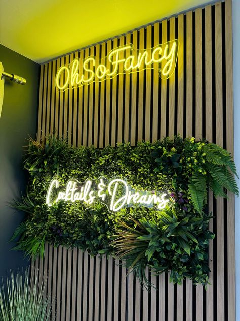 Grass Wall Bar, Plant Wall Office Interior Design, Wall Branding Ideas, Plant Wall With Neon Sign, Selfie Wall Ideas Salon, Faux Plant Wall With Neon Sign, Neon Logo Design, Foliage Wall With Neon Sign, Indoor Foliage Brick Wall Neon