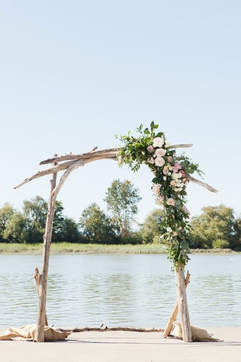 driftwood wedding arch with asymmetrical flower accent Driftwood Wedding Arch Diy, Driftwood Wedding Altar, Natural Wood Arbor, Driftwood Alter Wedding, Driftwood Wedding Arbor, Asymmetrical Wedding Arch Flowers, Driftwood Arbor Wedding, Drift Wood Wedding Arch, Lake Wedding Arch