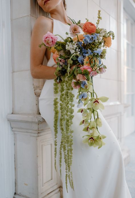 Elegant cascading wildflower bouquet held by the bride wearing a simple white wedding gown. Artistic Wedding Bouquets, Tulip And Wildflower Bouquet, Dangling Wedding Bouquet, Wildflower Wedding Bridesmaids Green, Flowy Wedding Bouquets, Colorful Cascading Bouquet, Colorful Cascade Wedding Bouquet, Wedding Cascading Bouquets, Wedding Bouquets Bride Cascade