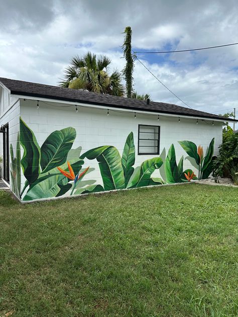 White guest house in a beautiful backyard has oversized tropical leaves painted on it the cinderblock wall, the leaves are vibrant shades of green and has a few birds of paradise woven in between for a pop of color. The leaves mural covers about two thirds of the wall space. Grass is seen in the foreground. Background leaves are painted as a silhouette. Backyard Mural, Painted Signage, Mural Artist, Atlanta Artist, Tropical Leaves, Custom Sign, Atlanta, Original Artwork, Mural