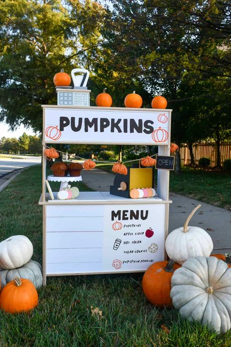 Decorated pumpkin stand made from the Ikea play kitchen. Has toys on it and pumpkins around it. Fall Lemonade Stand, Ikea Duktig Hack, Ikea Duktig Kitchen, Pumpkin Menu, Fall Bake Sale, Apple Cider Cookies, Stall Decorations, Farmers Market Stand, Pumpkins For Sale