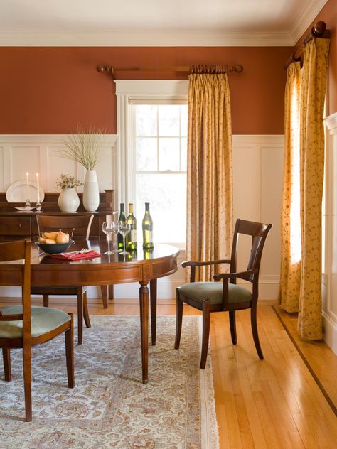 This traditional style dining room features white wainscoting below burnt sienna walls for a bright but earthy feel. Pale yellow curtains continue the warm theme. Victorian Dining Room Decor, Orange Dining Room, Burnt Orange Living Room, Wainscoting Living Room, Wainscoting Kitchen, Wainscoting Bedroom, Dining Room Victorian, Dining Room Wainscoting, Wainscoting Styles