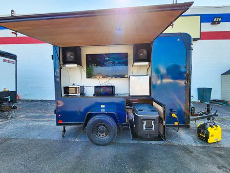 This 5’x10′ custom tailgate trailer has everything you need to be the star of the tailgate. With a large flip-up window revealing a 50-inch TV, dual Bluetooth speakers, a slide-out cooler, mini fridge, and microwave, plus an 18.5″ classic Pit Barrel drum cooker, 2-burner Camplux griddle, a bags set, a 10×10 pop-up tent, tables and chairs, a portable satellite dish, portable generator, and plenty of exterior lighting, it’s self-contained and ready for action! Tailgate Trailer, Tailgating Trailers, Window Reveal, Trailer Diy, Satellite Dish, Portable Generator, Tables And Chairs, Pop Up Tent, Mini Fridge