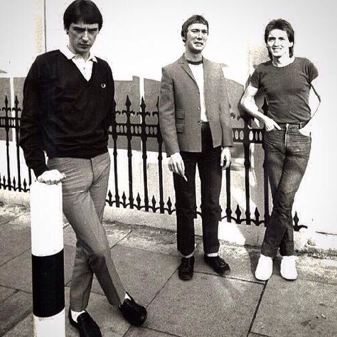 three men standing on the sidewalk next to a fence with a pole in front of them